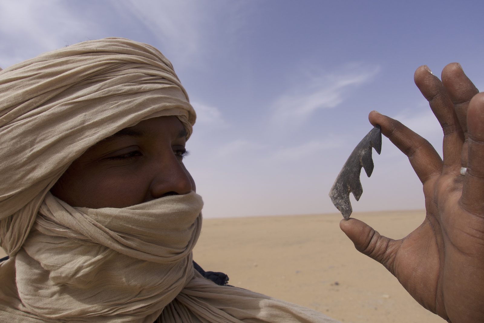 A hand holding a stone tool against a desert sky
