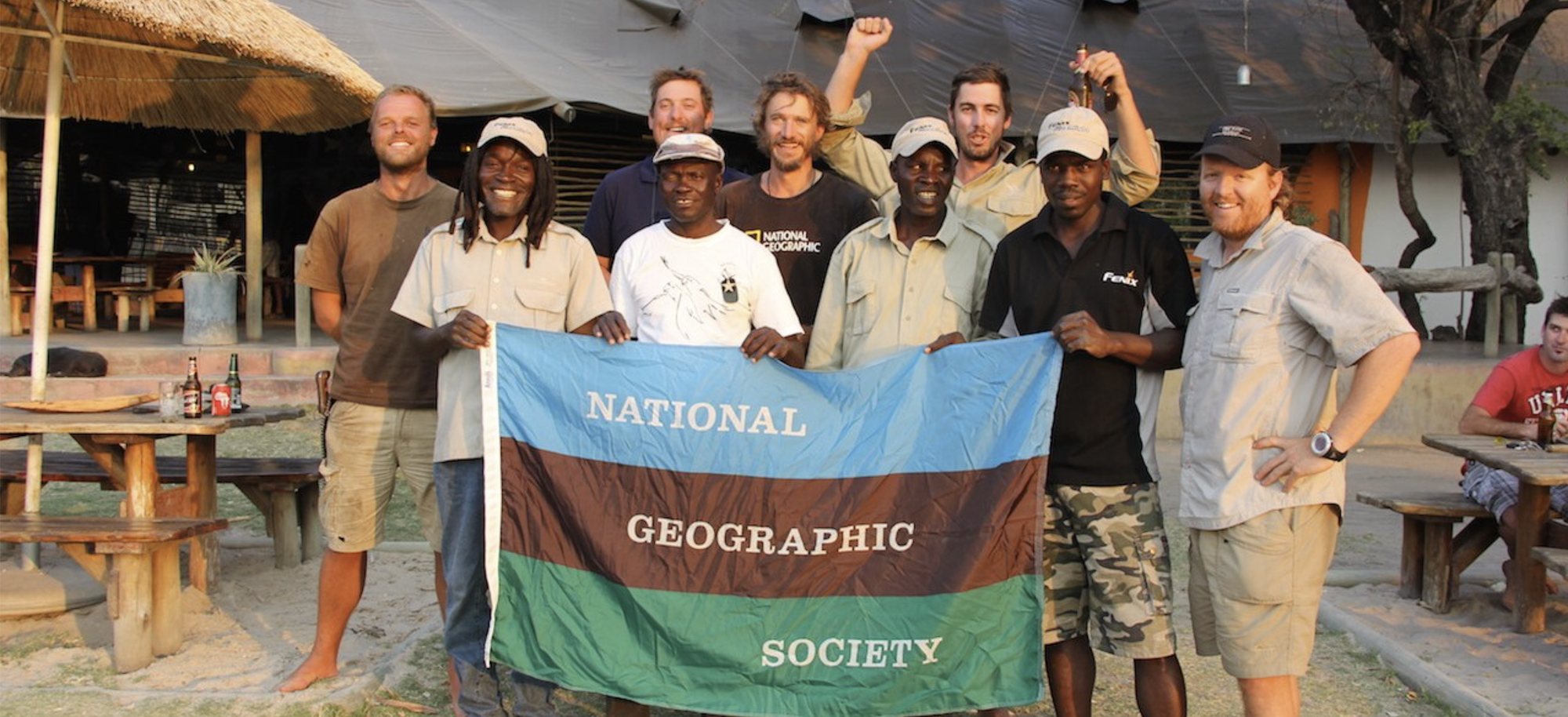 Paul Steyn with the National Geographic Society expedition team, holding the Society flag at a field camp